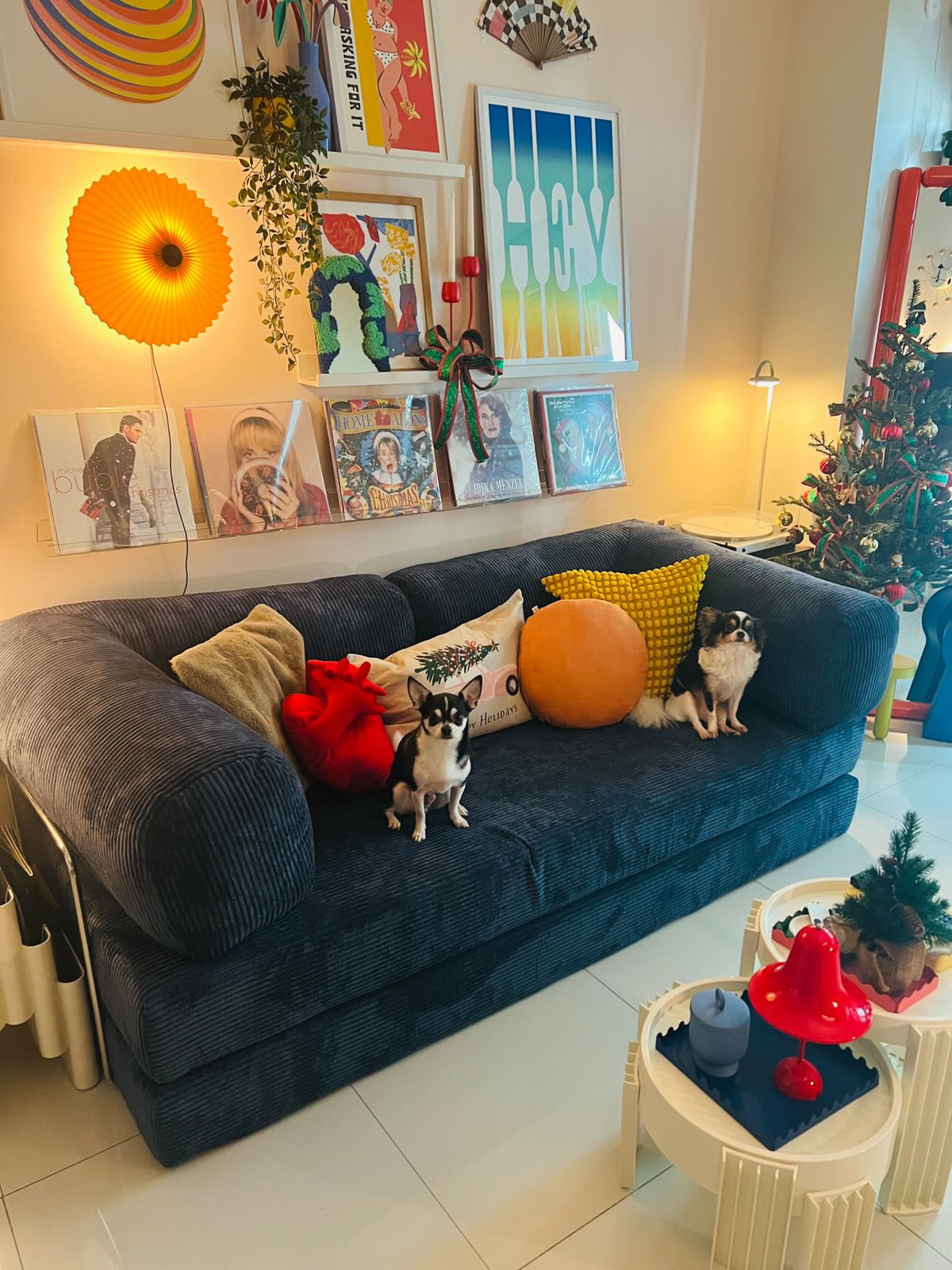 Modern living room with a blue Teddy sofa styled with colorful accent pillows, two small dogs, vibrant wall art, vinyl record display, and playful decor from Home Hue